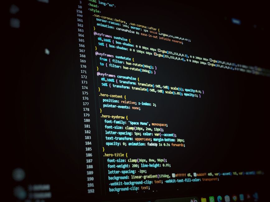 A close-up photograph of a computer screen displaying lines of code in a text editor, with syntax highlighting in various colors such as blue, yellow, and white on a dark background. The code includes