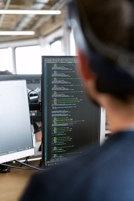 A close-up photograph of a computer screen displaying lines of code in a text editor, with syntax highlighting in various colors such as blue, yellow, and white on a dark background. The code includes